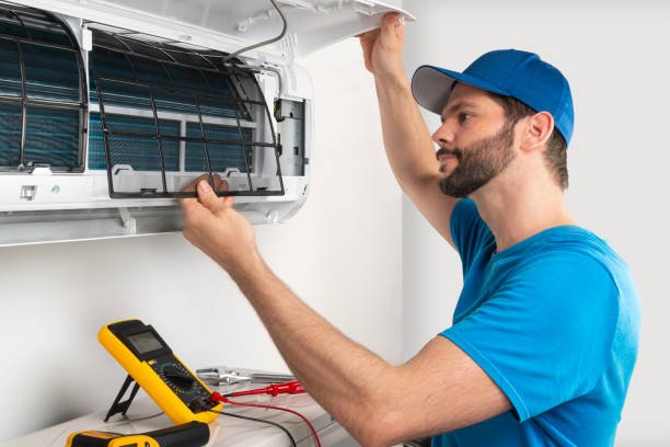 Installation service fix  repair maintenance of an air conditioner indoor unit, by cryogenist technican worker checking the air filter in blue shirt and baseball cap