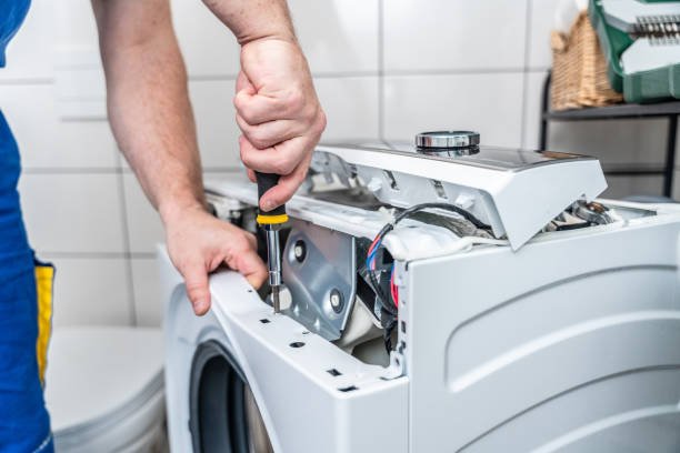 Repairman using a screwdriver disassembles a washing machine for repair